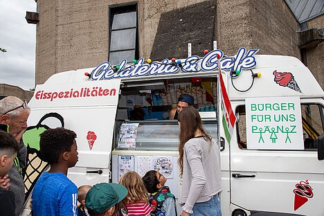 Die Kinder freuen sich auf die traditionelle Eiswagen-Aktion Kinder stehen vor einem Eiswagen und freuen sich auf die Ausgabe von Eis.
